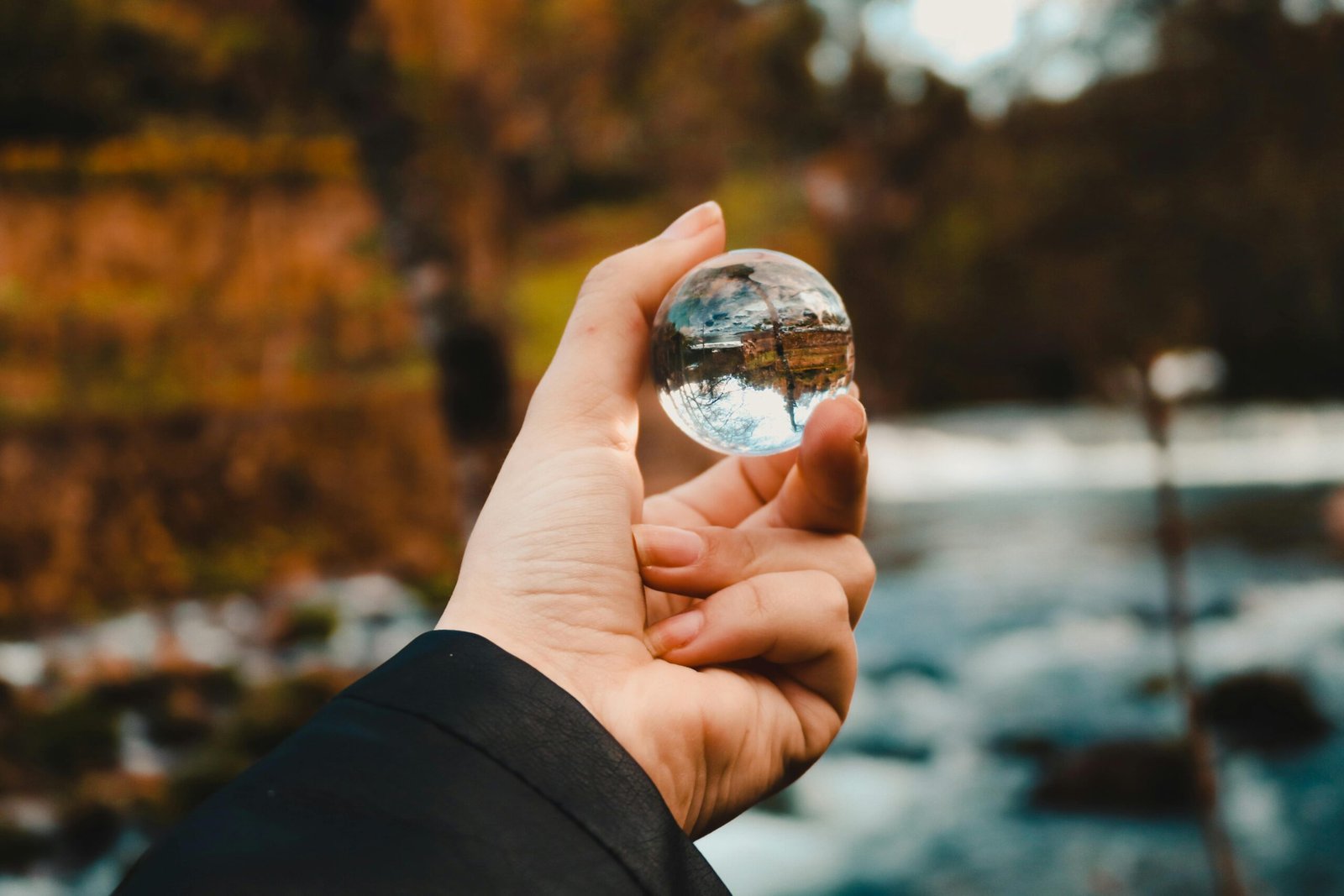 A hand holds a crystal ball, reflecting a vibrant autumn landscape.